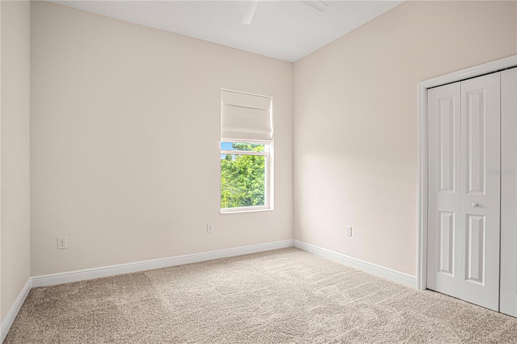 A bedroom with beige walls, beige carpeting, a single window, and white closet doors — 2938 SERENO POINTE DRIVE, TITUSVILLE, FL