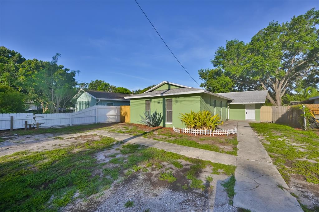 A green single-story house with a white fence and a concrete walkway in the yard — 15616 AVALON AVENUE UNIT 1, CLEARWATER, FL
