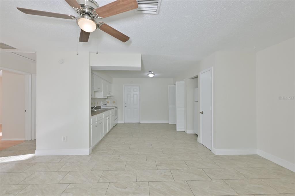 A kitchen with white cabinets and tile flooring opens into a living area with a fan — 15616 AVALON AVENUE UNIT 1, CLEARWATER, FL