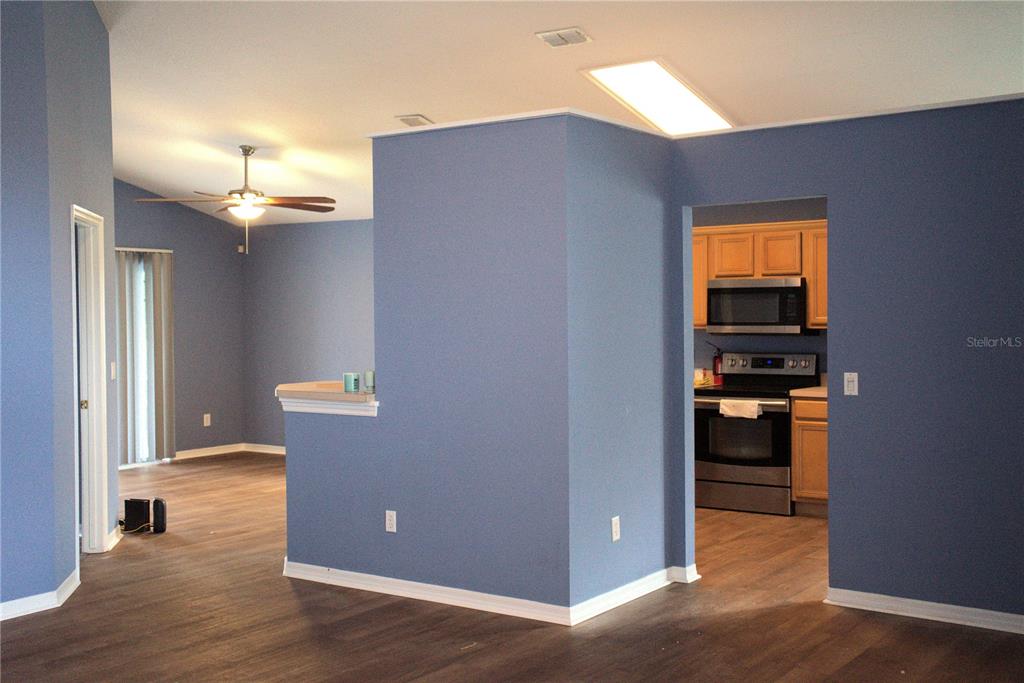 A blue-walled living area with wood-look flooring leads into a kitchen with wooden cabinets — 209 WESTMORELAND CIRCLE, KISSIMMEE, FL