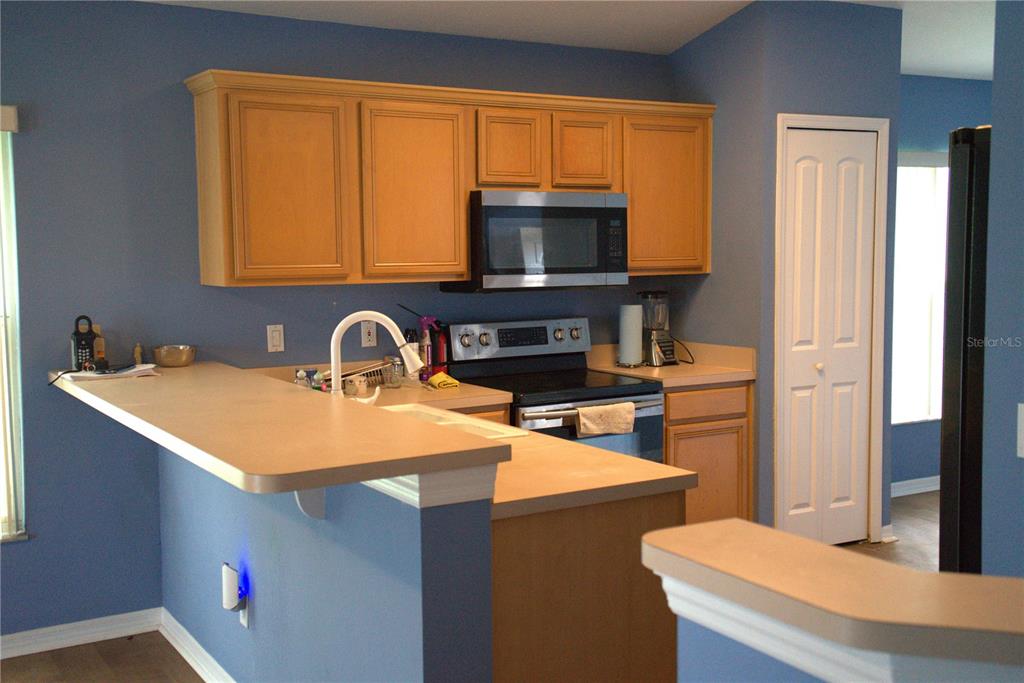A kitchen features blue walls, light wood cabinets, laminate countertops, and stainless steel appliances — 209 WESTMORELAND CIRCLE, KISSIMMEE, FL