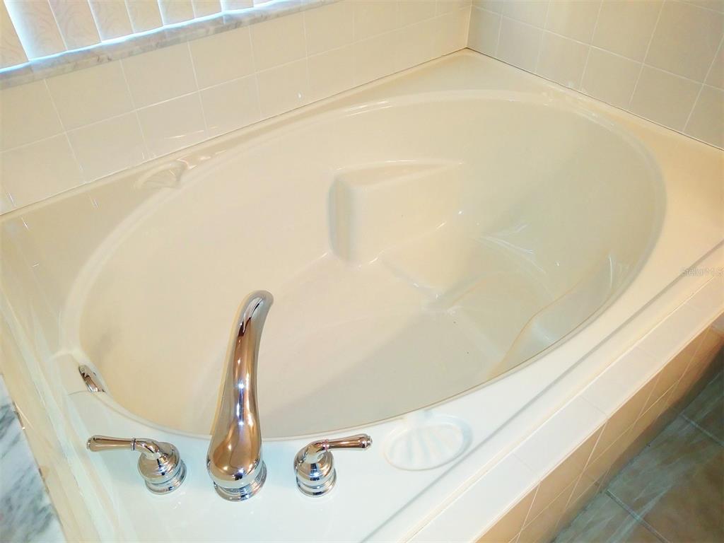 A built-in oval soaking tub with chrome fixtures and white tile surround in a bathroom — 209 WESTMORELAND CIRCLE, KISSIMMEE, FL