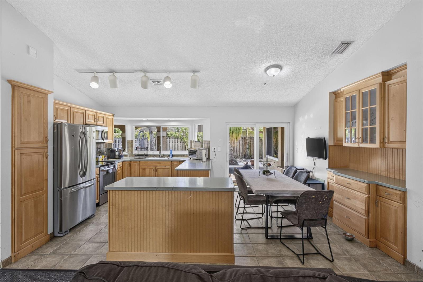 A kitchen and dining area features light wood cabinetry, stainless steel appliances, and tile flooring — 2171 Amesbury Circle, Wellington FL 33414, WELLINGTON, FL