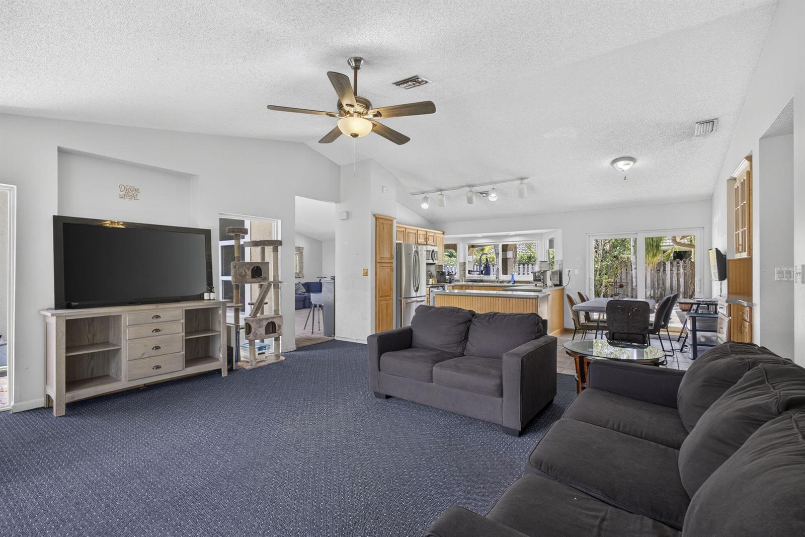 A living room with blue carpet, dark gray sofas, and an open kitchen in the background — 2171 Amesbury Circle, Wellington FL 33414, WELLINGTON, FL