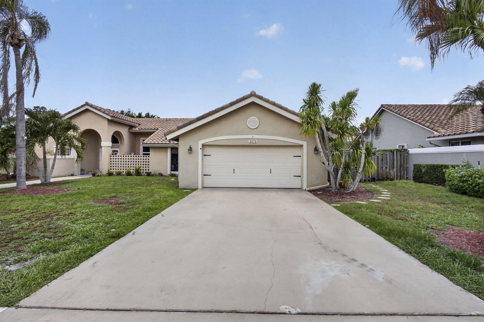 A single-story house with a beige stucco exterior, a tile roof, and a concrete driveway — 2171 Amesbury Circle, Wellington FL 33414, WELLINGTON, FL