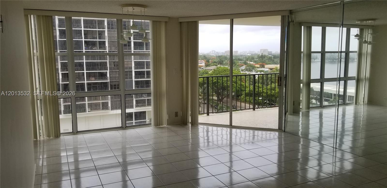 A bright living room features white tile floors, floor-to-ceiling windows, and a balcony with views — 1901 Brickell Ave # B906, Miami FL 33129, MIAMI, FL