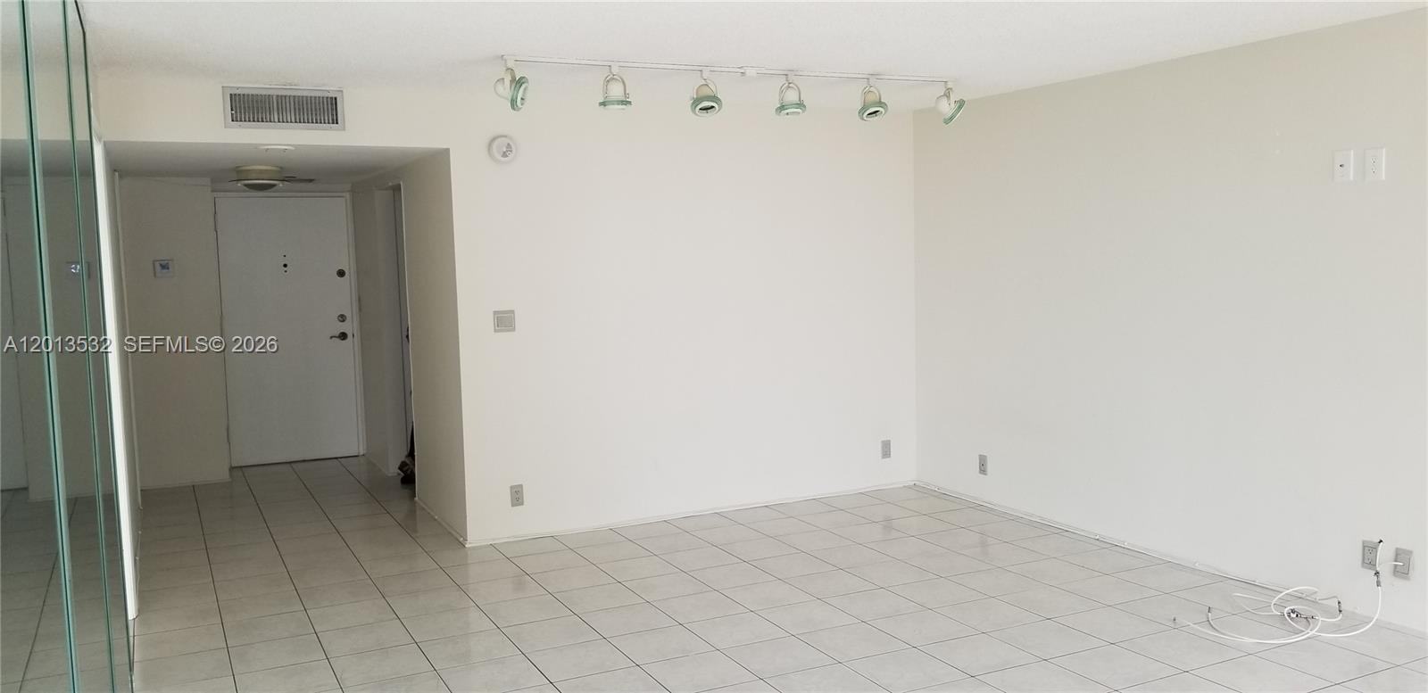 An empty room features white walls, light-colored tile flooring, and a track lighting system — 1901 Brickell Ave # B906, Miami FL 33129, MIAMI, FL