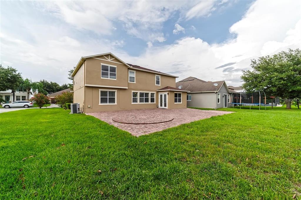 The rear exterior of a two-story tan house features a brick paver patio — 10124 MALPAS POINT, ORLANDO, FL