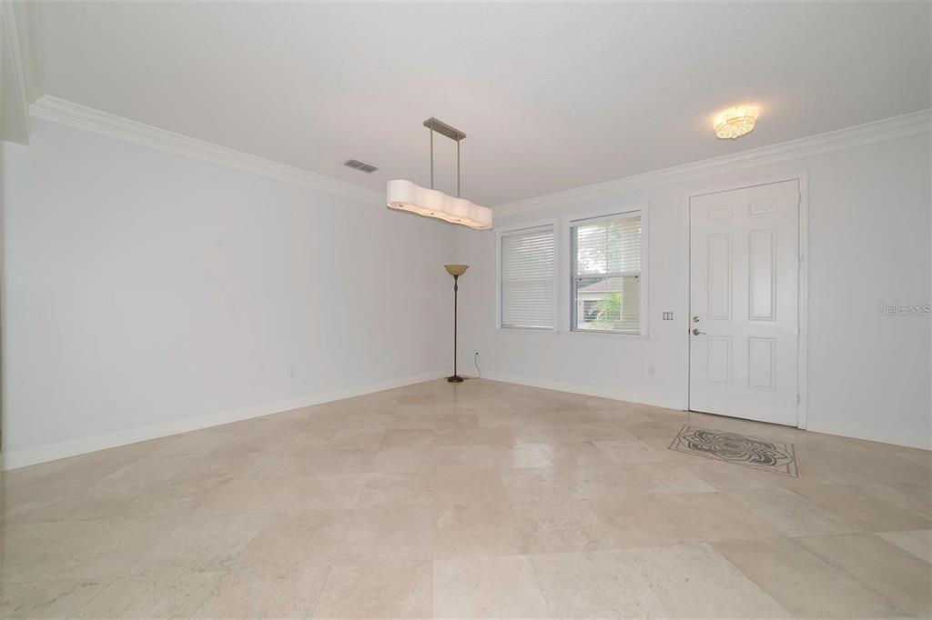 A bright, empty room features light-colored tile floors, a modern chandelier, and a white door — 10124 MALPAS POINT, ORLANDO, FL