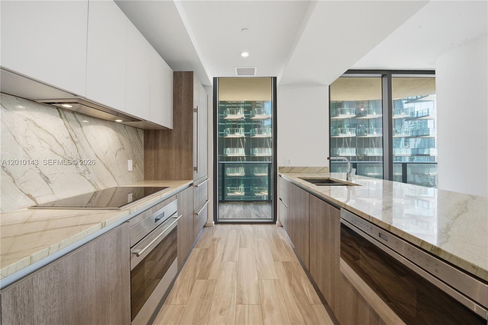A modern galley kitchen features wood-toned cabinetry, marble countertops, and a balcony view — 801 S Miami Ave # 2505, Miami FL 33130, MIAMI, FL