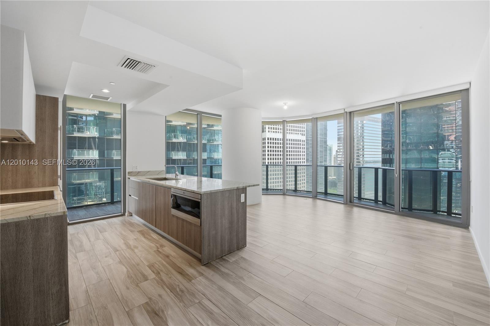 A modern kitchen with wood cabinetry and an island opens into a bright living area — 801 S Miami Ave # 2505, Miami FL 33130, MIAMI, FL