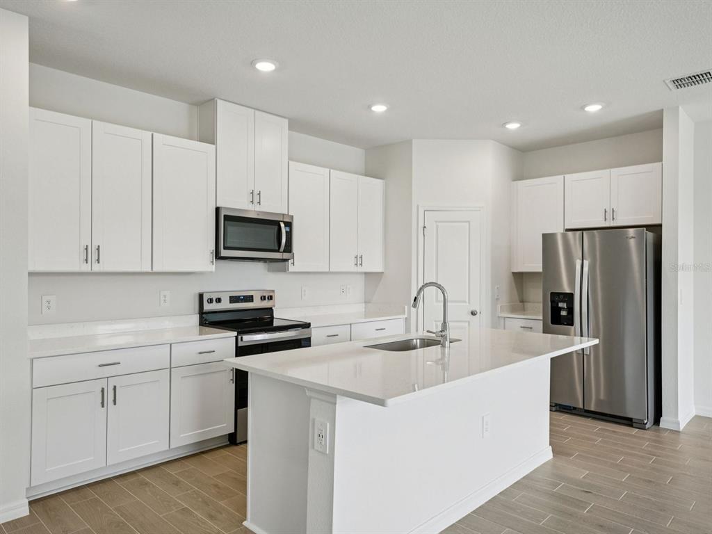 A modern kitchen features white cabinetry, stainless steel appliances, and a central island with countertops — 12556 HOMELAND DRIVE, DADE CITY, FL