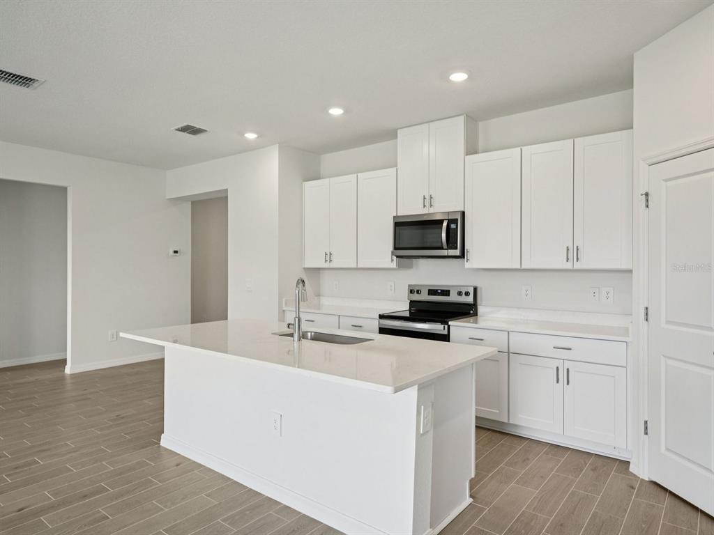 A modern kitchen features white cabinets, a central island with a sink, and stainless appliances — 12556 HOMELAND DRIVE, DADE CITY, FL