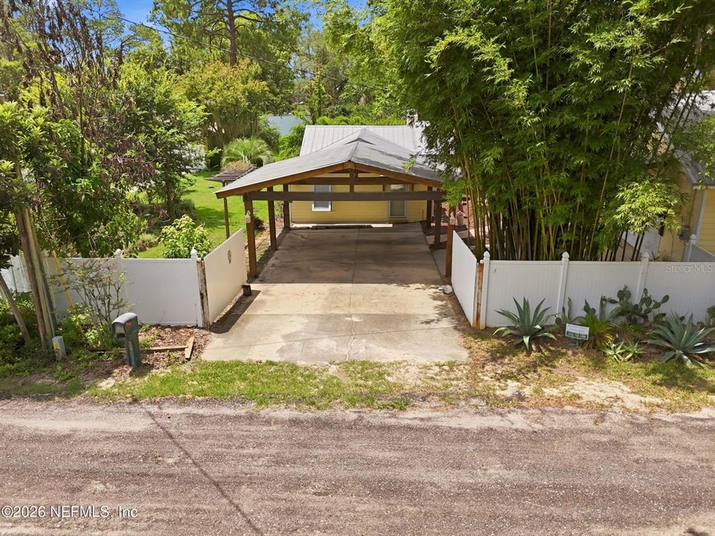 A yellow house features a large wooden carport and a white vinyl privacy fence — 7932 BREEZY POINT ROAD W, MELROSE, FL