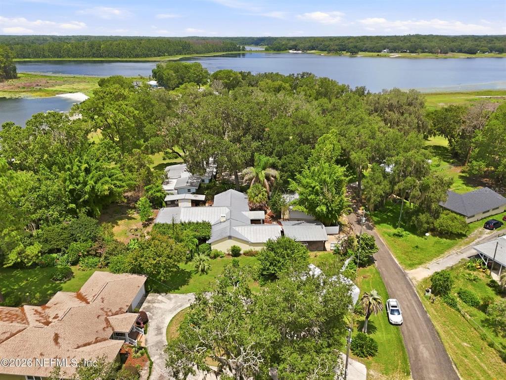 An aerial view shows a house with a metal roof surrounded by trees near a lake — 7932 BREEZY POINT ROAD W, MELROSE, FL