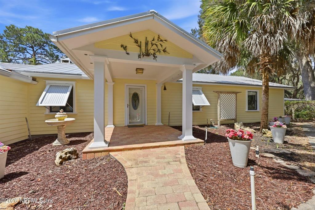 A yellow house features a covered front porch with white columns and a brick walkway — 7932 BREEZY POINT ROAD W, MELROSE, FL