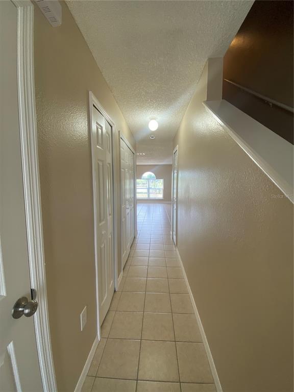 A narrow hallway with beige walls, tile flooring, and white doors leads toward a window — 30302 DOUBLE DRIVE, WESLEY CHAPEL, FL