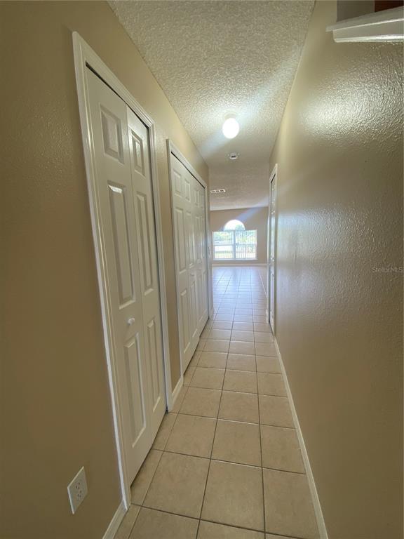 A hallway with tiled floors and white closet doors leads toward a bright living area — 30302 DOUBLE DRIVE, WESLEY CHAPEL, FL