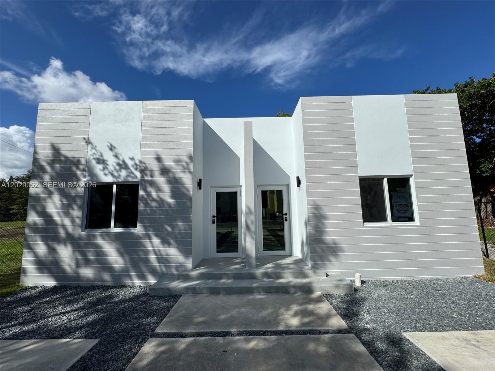 A modern, single-story duplex with gray horizontal siding, white accents, and two glass entry doors — 135 NW 60th St # B, Miami FL 33127, MIAMI, FL
