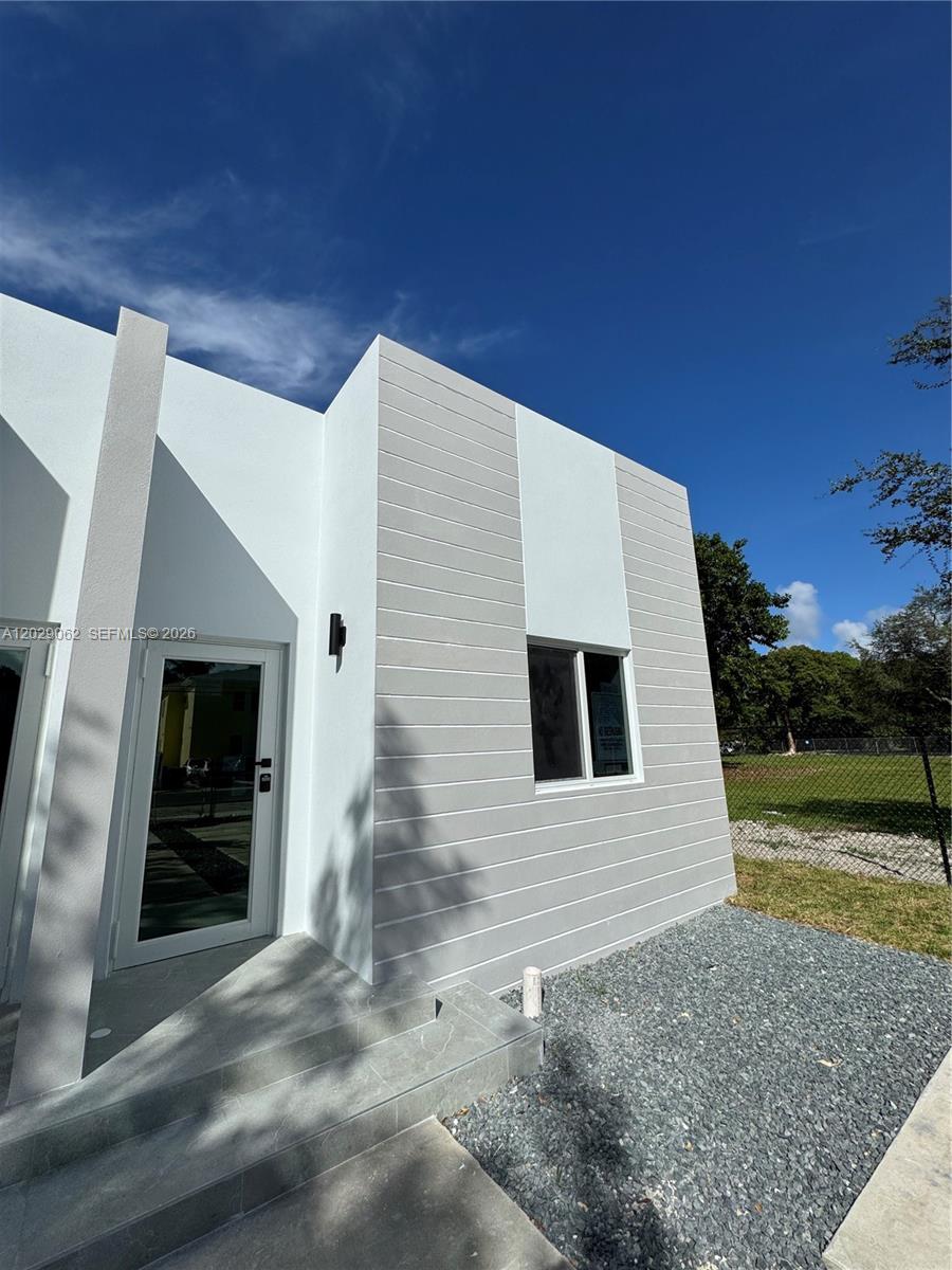 A modern white building exterior features horizontal siding, a glass door, and a gravel yard — 135 NW 60th St # B, Miami FL 33127, MIAMI, FL