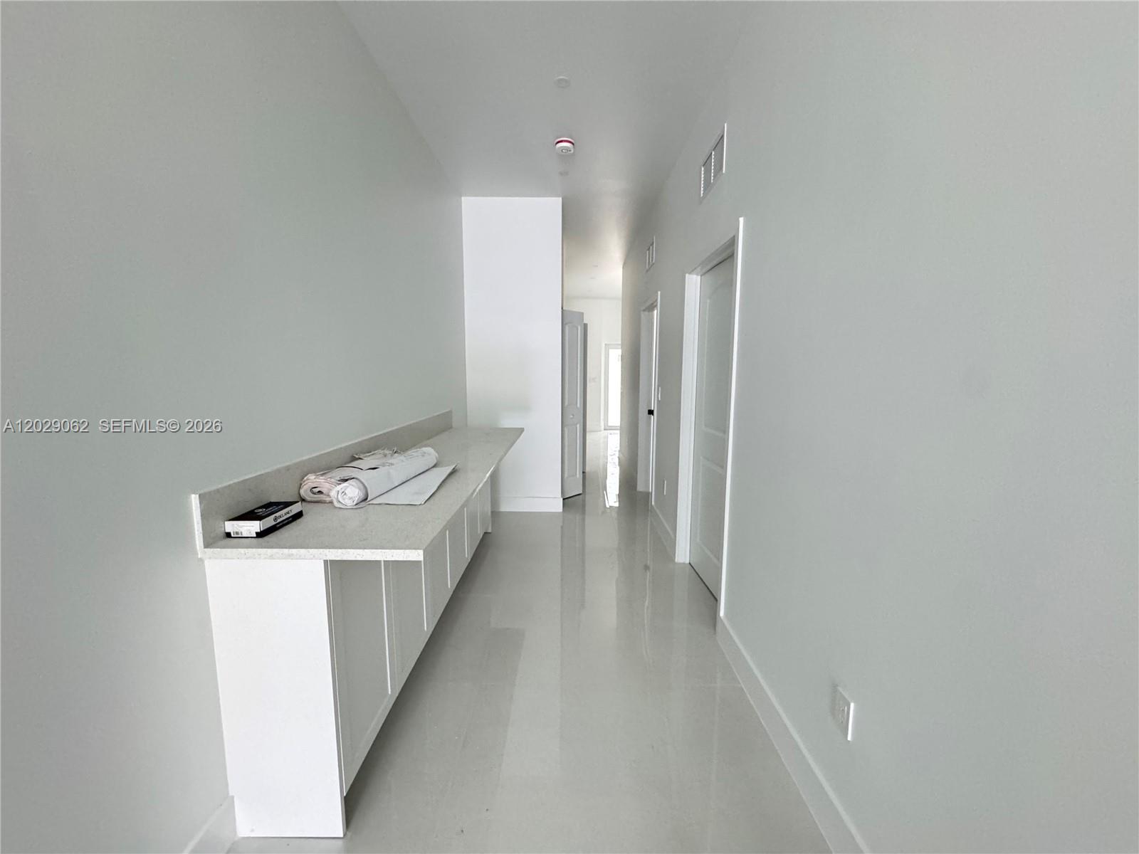 A hallway features white walls, light tile flooring, and a long built-in white cabinet counter — 135 NW 60th St # B, Miami FL 33127, MIAMI, FL