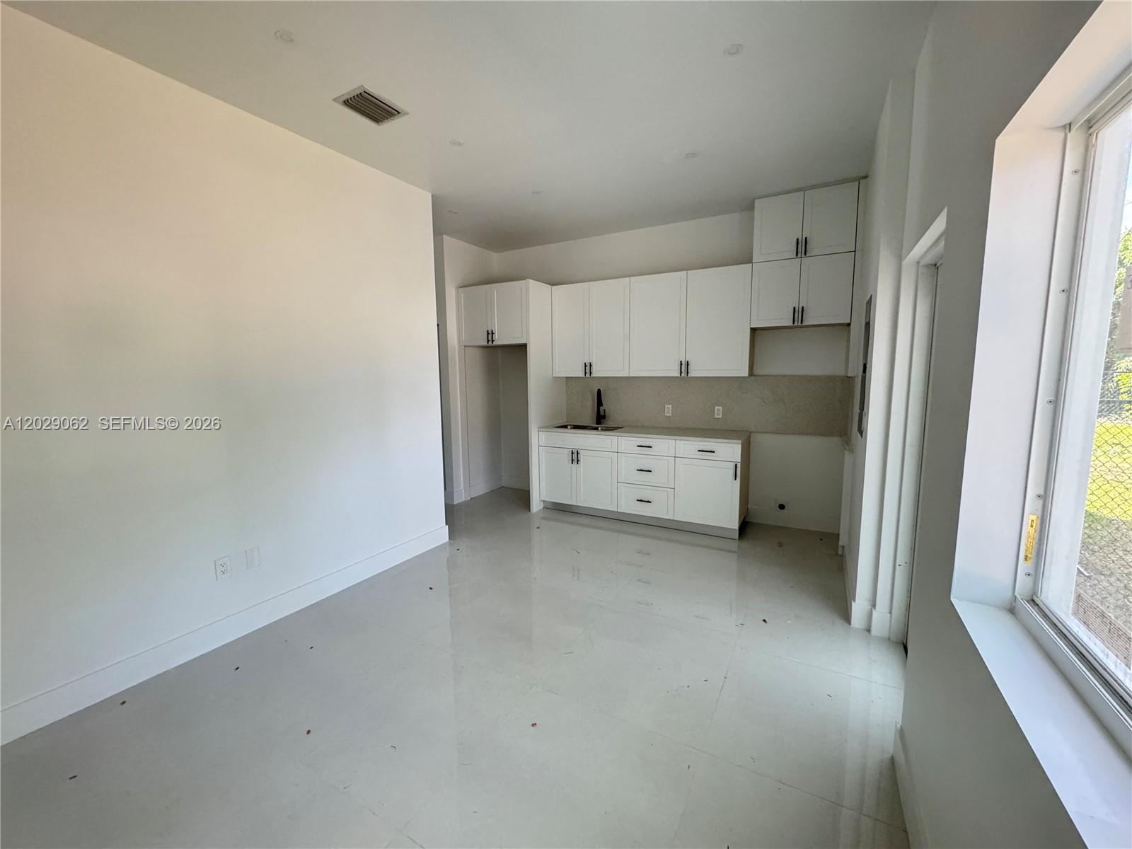 A kitchen with white cabinets, light tile flooring, and a window on the right — 135 NW 60th St # B, Miami FL 33127, MIAMI, FL