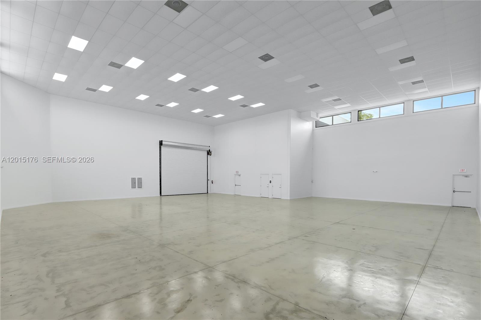 A large, empty warehouse space features white walls, a concrete floor, and a roll-up door — 6767 NE 2nd ave, Miami FL 33138, MIAMI, FL