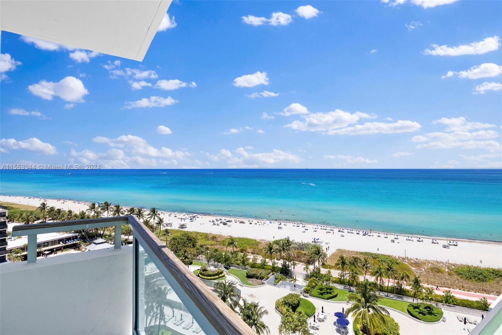 A high-angle view from a balcony overlooking a sandy beach, ocean, and tropical landscaping — 5151 Collins Ave # 1527, Miami Beach FL 33140, MIAMI BEACH, FL
