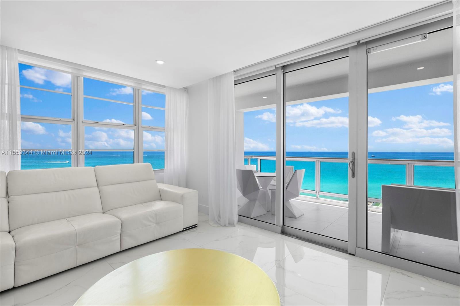 A white living room features a leather sofa, gold coffee table, and balcony with ocean views — 5151 Collins Ave # 1527, Miami Beach FL 33140, MIAMI BEACH, FL