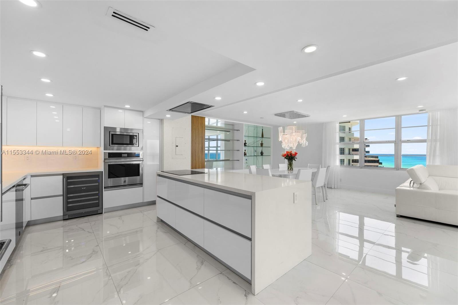 A modern white kitchen features a large island, marble floors, and ocean views — 5151 Collins Ave # 1527, Miami Beach FL 33140, MIAMI BEACH, FL