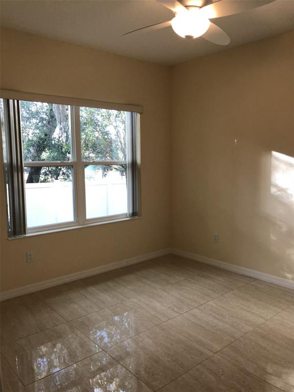 An empty room features beige walls, large light-colored floor tiles, and a ceiling fan — 2036 ROYAL VISTA COURT, ORLANDO, FL