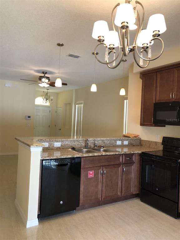 A kitchen features dark wood cabinets, granite countertops, black appliances, and a chandelier — 2036 ROYAL VISTA COURT, ORLANDO, FL