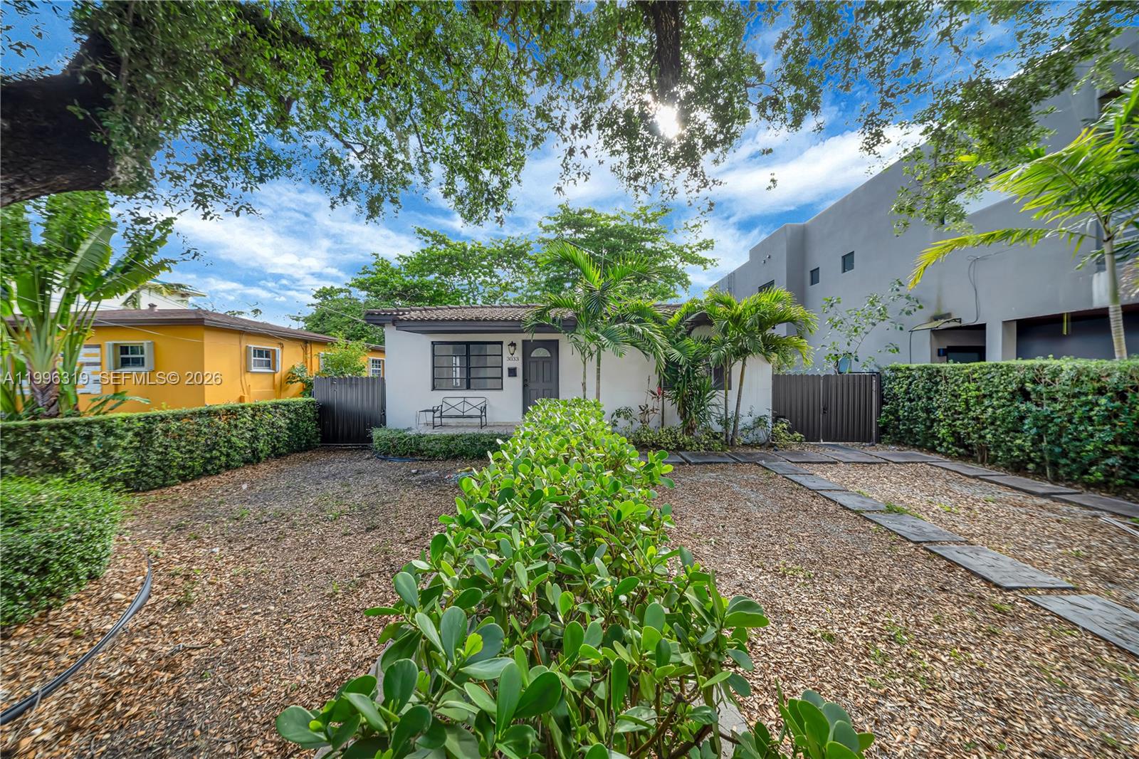 A white single-story house features a gravel front yard, a central hedge, and palm trees — 3033 Hibiscus St, Miami FL 33133, MIAMI, FL