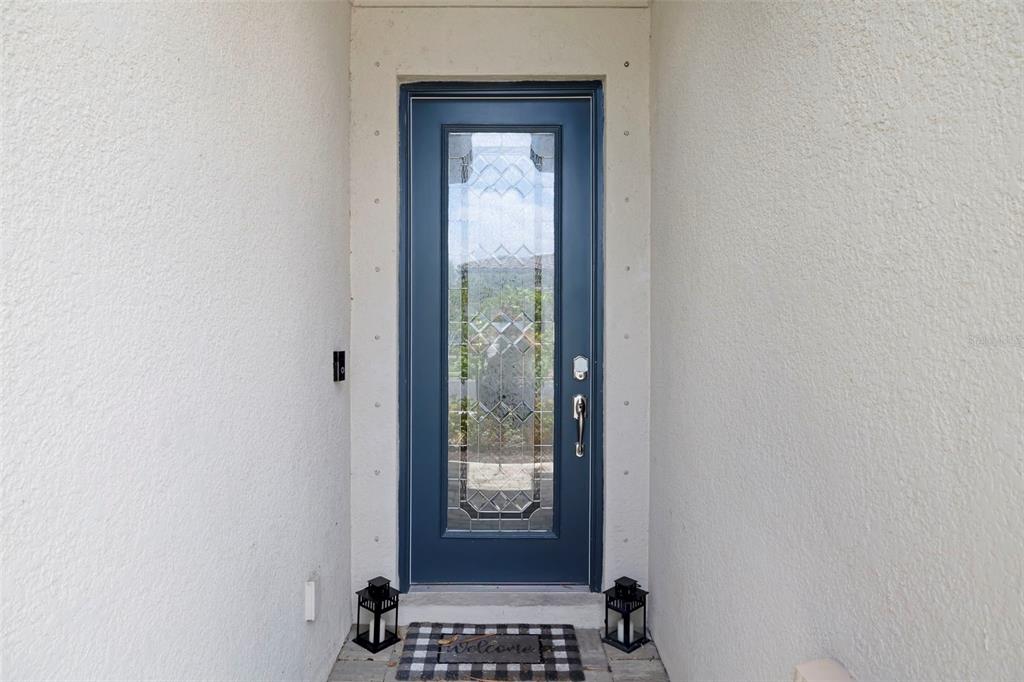 A blue front door with a glass insert is centered between two lanterns and a mat — 17927 POLO TRAIL, BRADENTON, FL