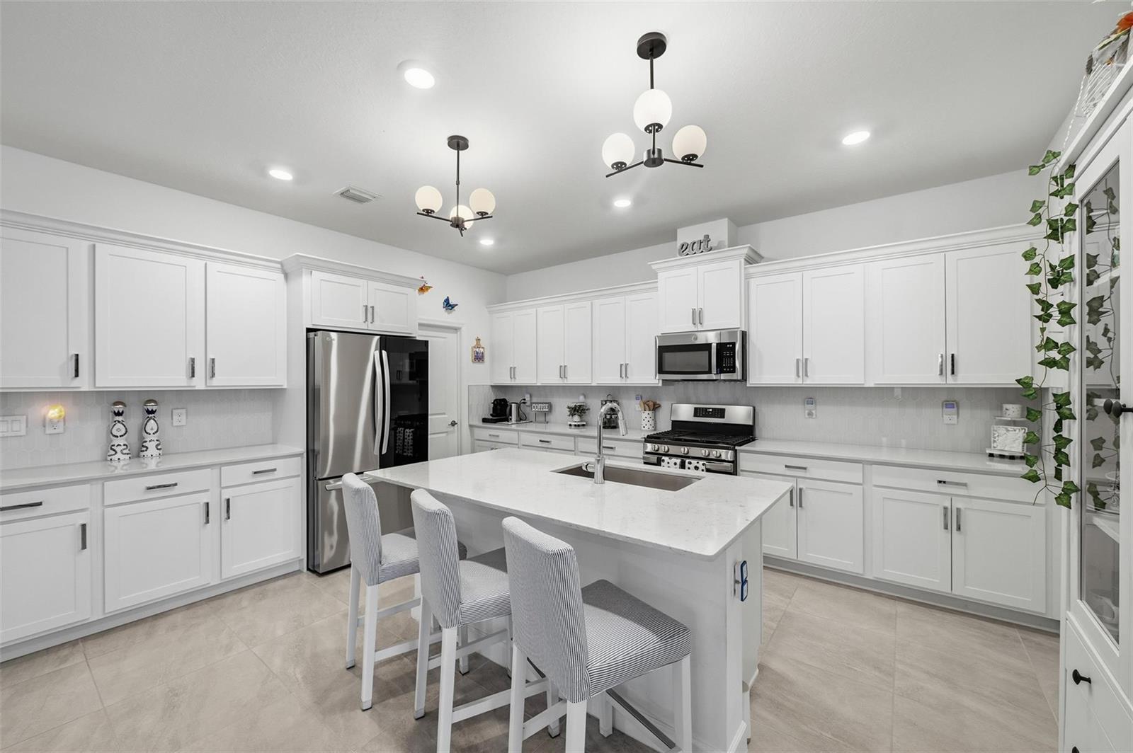 A bright kitchen features white cabinetry, stainless steel appliances, a central island, and pendant lighting — 1279 Tangled Orchard Trace # 1279, Loxahatchee FL 33470, LOXAHATCHEE, FL