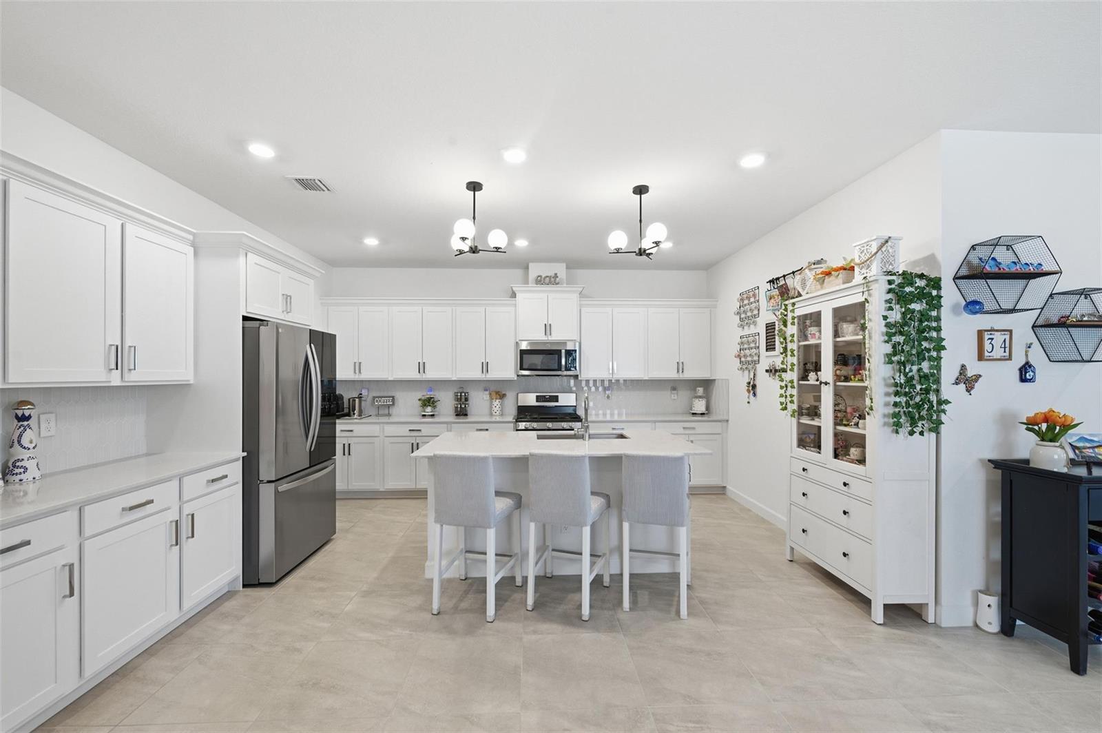 A bright, modern kitchen features white cabinetry, stainless steel appliances, and a central island — 1279 Tangled Orchard Trace # 1279, Loxahatchee FL 33470, LOXAHATCHEE, FL