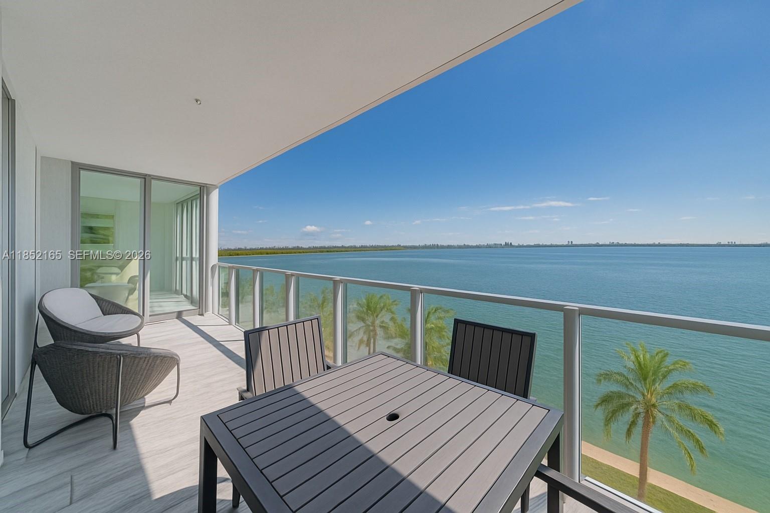 A balcony with outdoor furniture overlooks a large body of water and palm trees — 2900 NE 7th Ave # 405, Miami FL 33137, MIAMI, FL