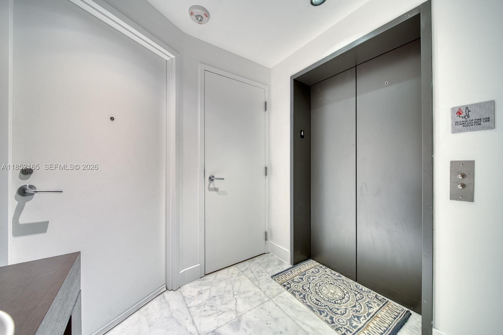 A hallway features a white door, a dark elevator door, and marble-style flooring — 2900 NE 7th Ave # 405, Miami FL 33137, MIAMI, FL