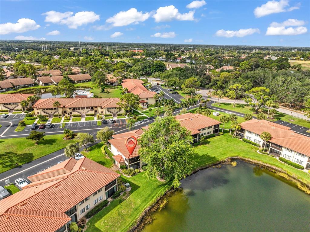 An aerial view shows a multi-story residential building with a red tile roof near a pond — 5221 LAKE VILLAGE DRIVE UNIT 24, SARASOTA, FL