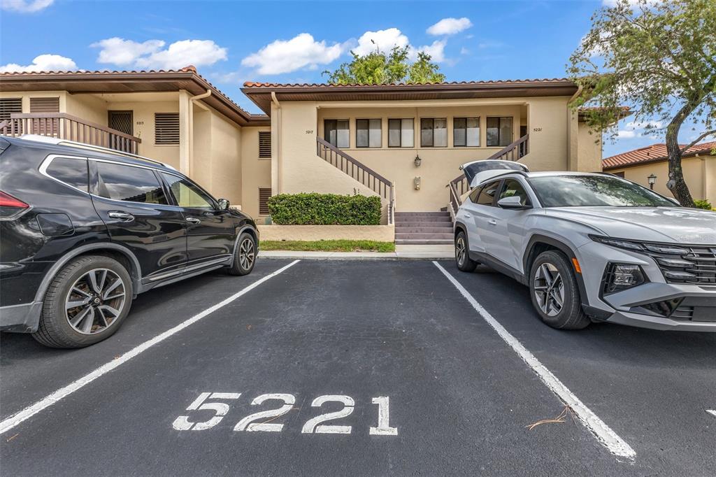 Two cars are parked in front of a two-story tan apartment building with stairs — 5221 LAKE VILLAGE DRIVE UNIT 24, SARASOTA, FL