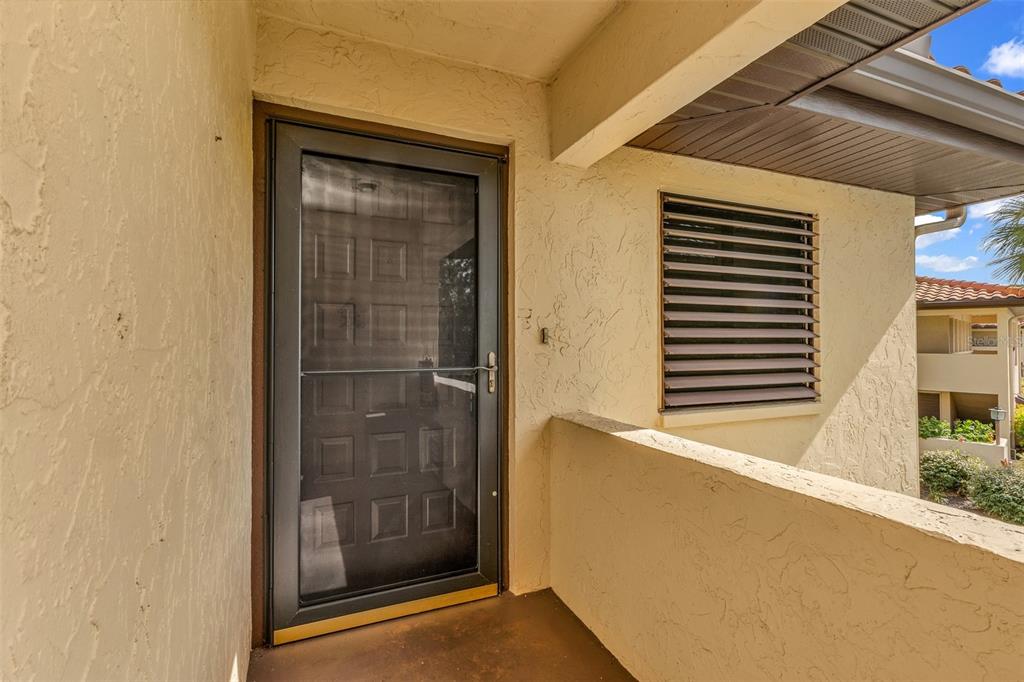 A view of a building exterior featuring a dark storm door and a louvered window — 5221 LAKE VILLAGE DRIVE UNIT 24, SARASOTA, FL