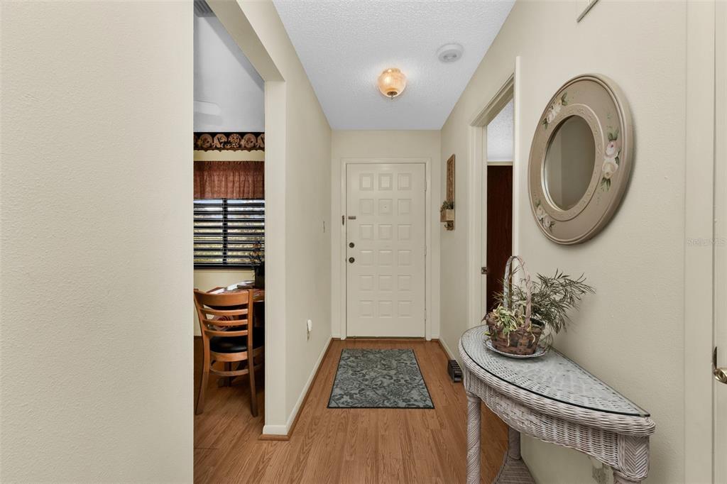 A foyer with wood-look flooring, a white front door, and a glass-topped wicker console table — 5221 LAKE VILLAGE DRIVE UNIT 24, SARASOTA, FL