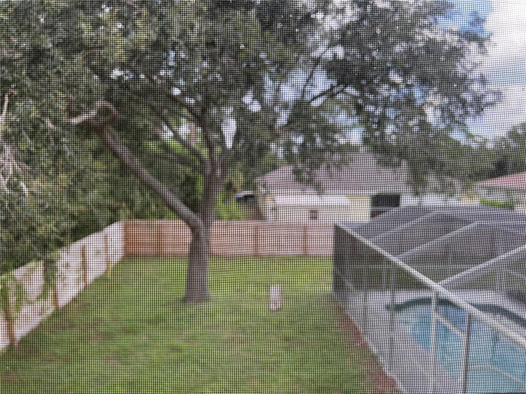 A view of a backyard with a large tree, a wooden fence, and a pool enclosure — 3774 LORTON AVENUE, NORTH PORT, FL