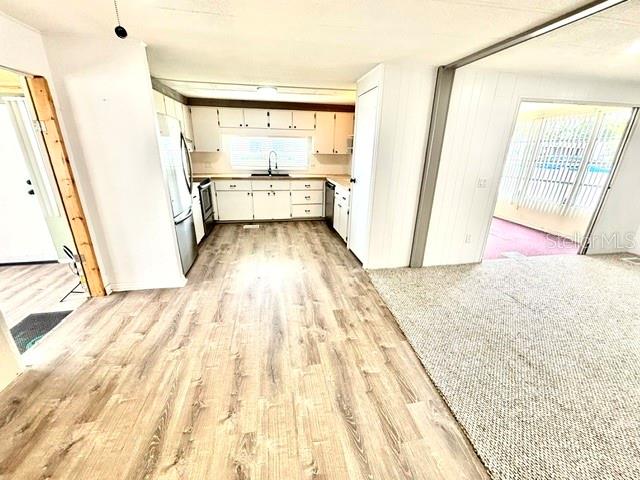 A kitchen with wood-look flooring and white cabinets connects to a carpeted living area — 106 ALOHA TERRACE, PORT ORANGE, FL