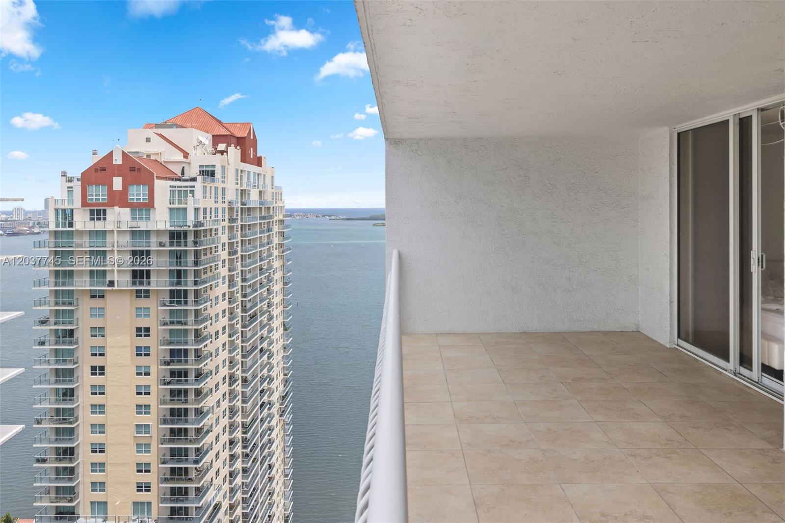 A balcony with tiled flooring overlooks a large body of water and a neighboring skyscraper — 1200 Brickell Bay Dr # 3714, Miami FL 33131, MIAMI, FL