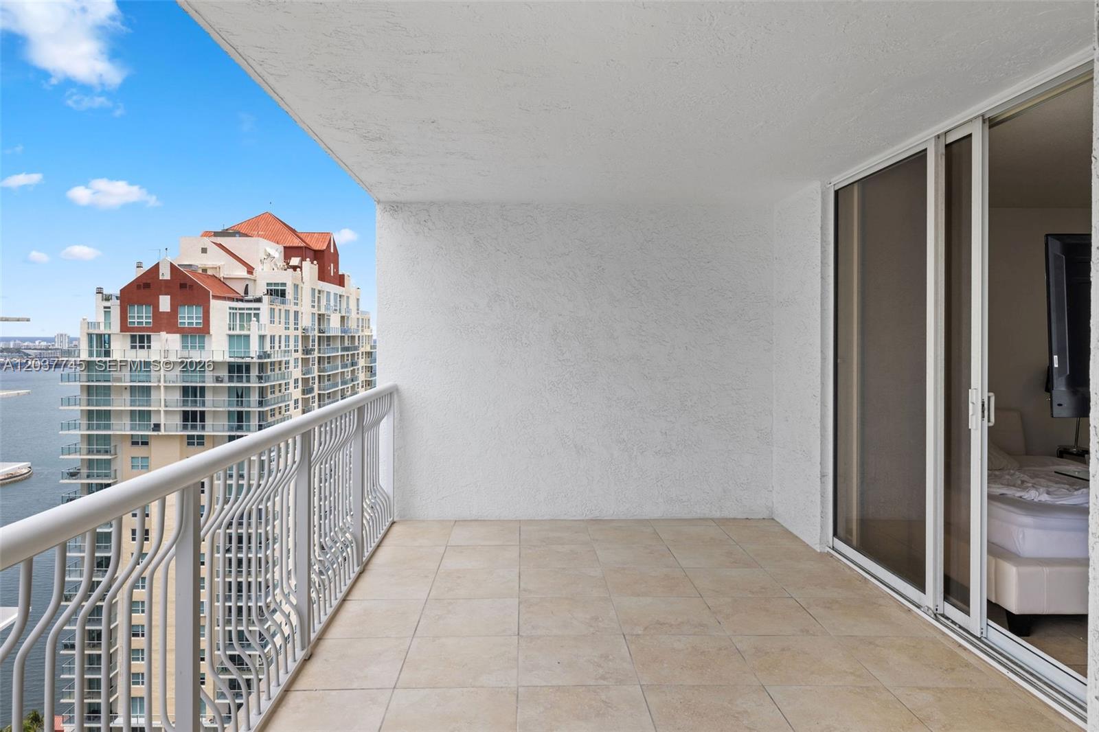 A balcony with beige tile flooring overlooks a large residential building and a body of water — 1200 Brickell Bay Dr # 3714, Miami FL 33131, MIAMI, FL