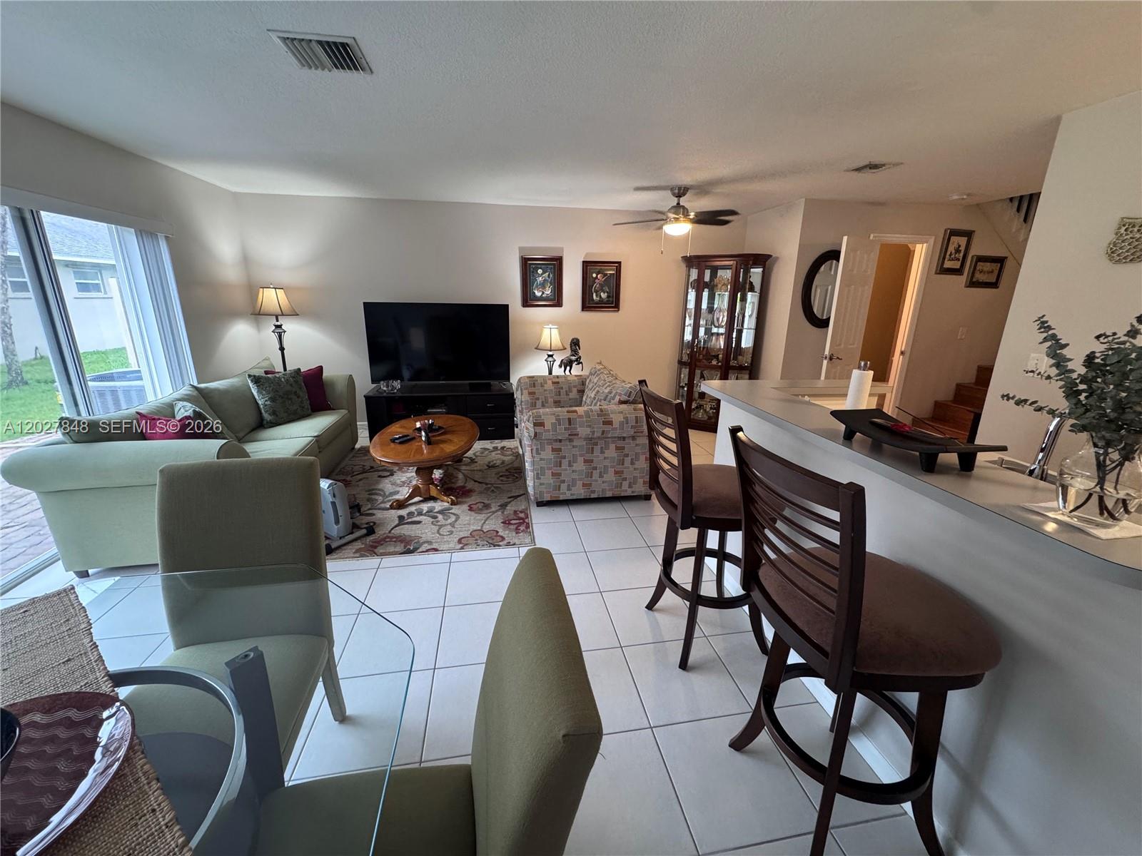 This living room features tile flooring, a breakfast bar with stools, and a glass-topped table — 12204 NW 36th Pl, Sunrise FL 33323, SUNRISE, FL
