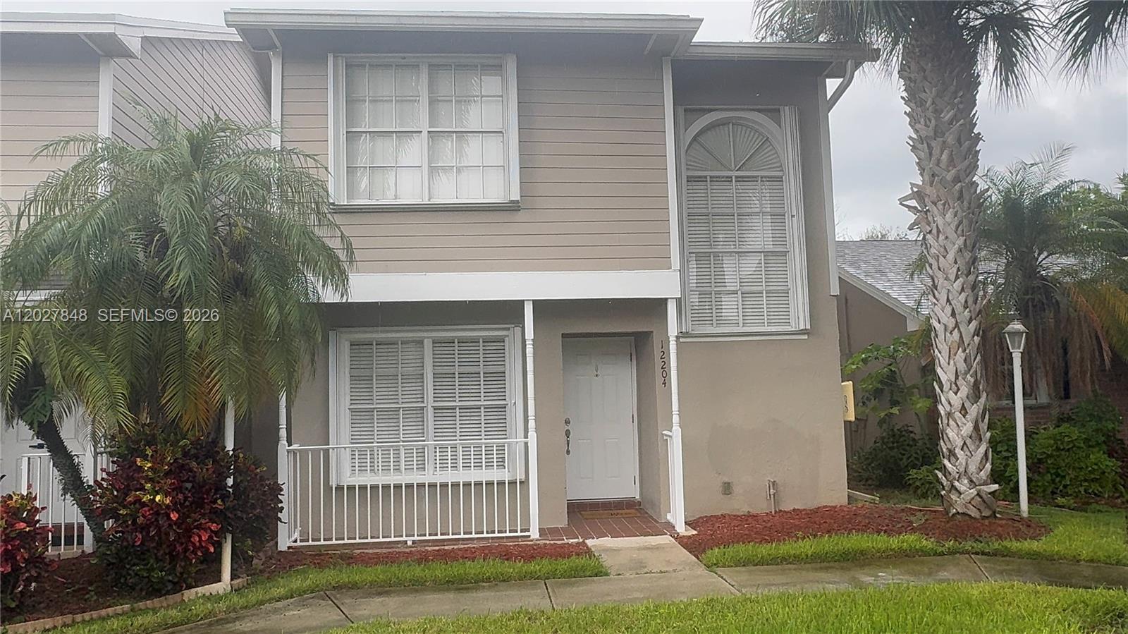 A two-story townhouse exterior features beige siding, white trim, and a palm tree — 12204 NW 36th Pl, Sunrise FL 33323, SUNRISE, FL