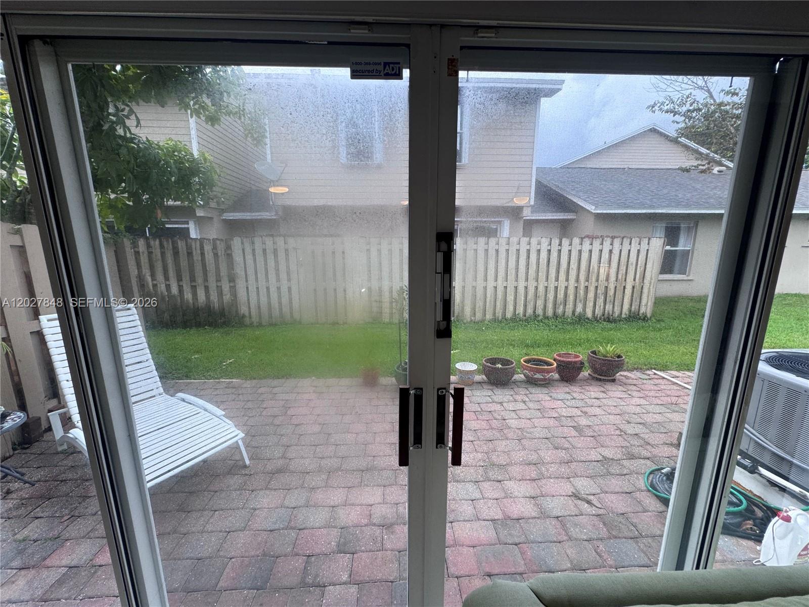 A view through sliding glass doors shows a brick patio, a white lounge chair, and a fence — 12204 NW 36th Pl, Sunrise FL 33323, SUNRISE, FL