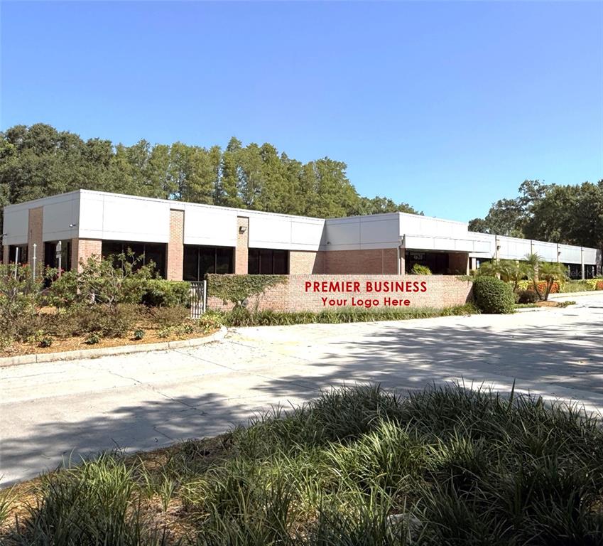 A low-rise brick and metal commercial building features a prominent sign on a brick wall — 4620 WOODLAND CORPORATE BOULEVARD, TAMPA, FL